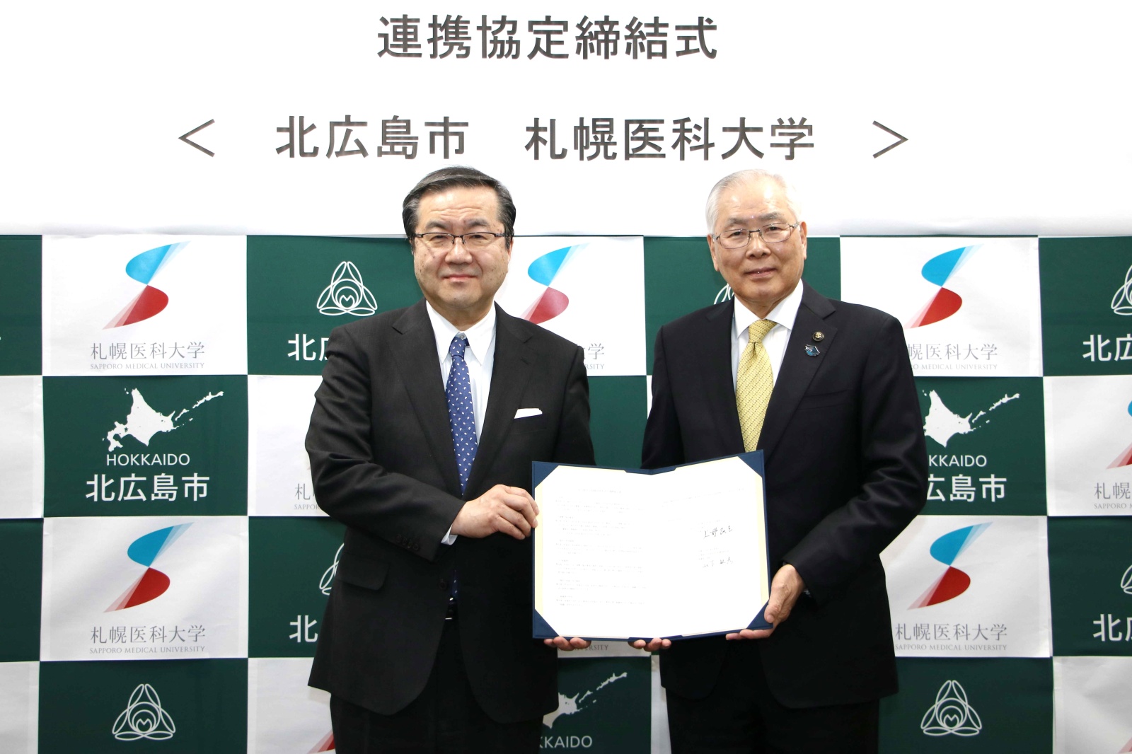 北広島市の上野市長と本学の山下理事長・学長が署名後の協定書を手に持っています。