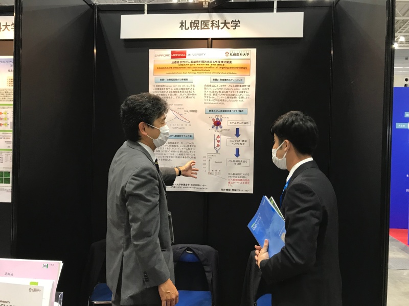 札幌医科大学展示ブースにて、来場者に研究内容を説明